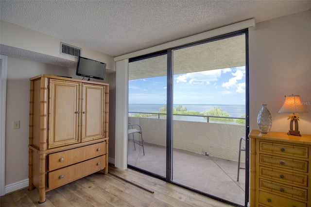 bedroom with a textured ceiling, light hardwood / wood-style flooring, and expansive windows