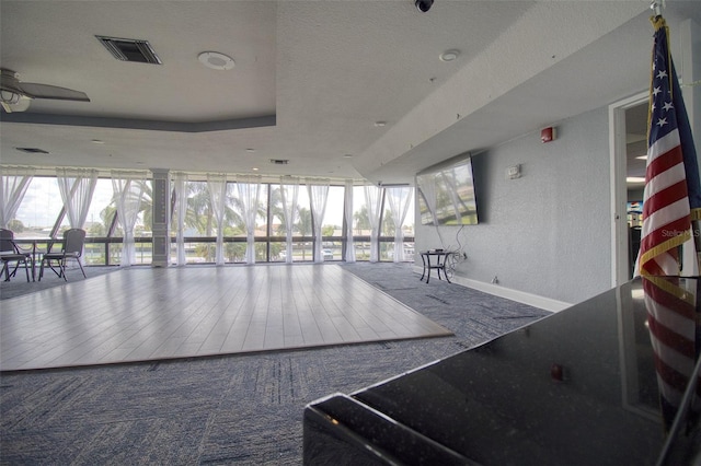 interior space with a wall of windows, ceiling fan, and a raised ceiling