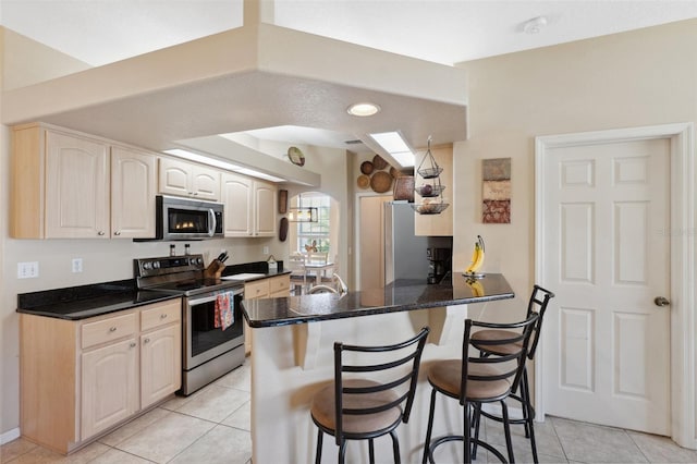 kitchen featuring kitchen peninsula, vaulted ceiling, a kitchen bar, appliances with stainless steel finishes, and light tile patterned flooring