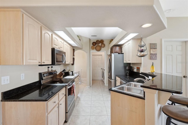 kitchen with a kitchen breakfast bar, stainless steel appliances, kitchen peninsula, light tile patterned floors, and sink