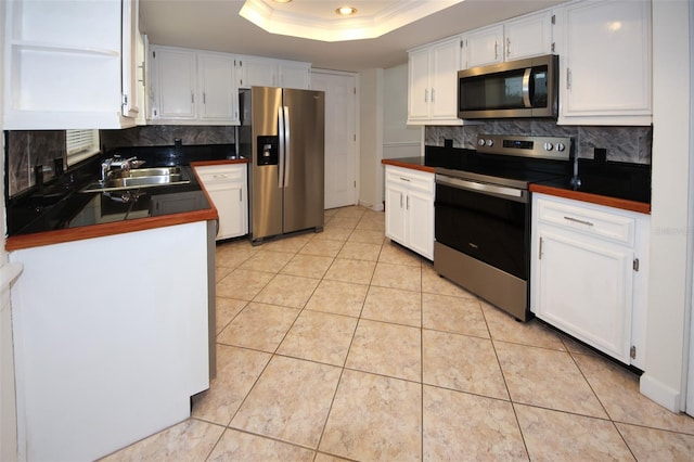 kitchen featuring appliances with stainless steel finishes, tasteful backsplash, a tray ceiling, sink, and white cabinetry