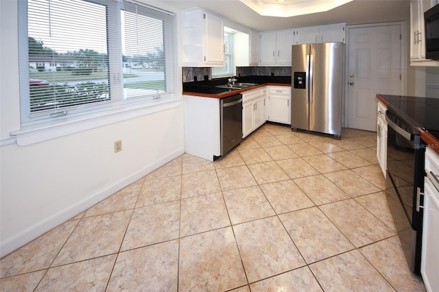 kitchen featuring black appliances, sink, light tile patterned floors, a tray ceiling, and white cabinetry