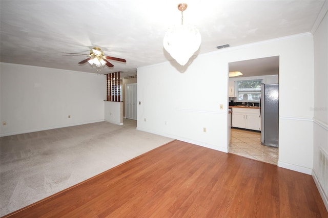 unfurnished living room featuring light carpet, ceiling fan, and ornamental molding