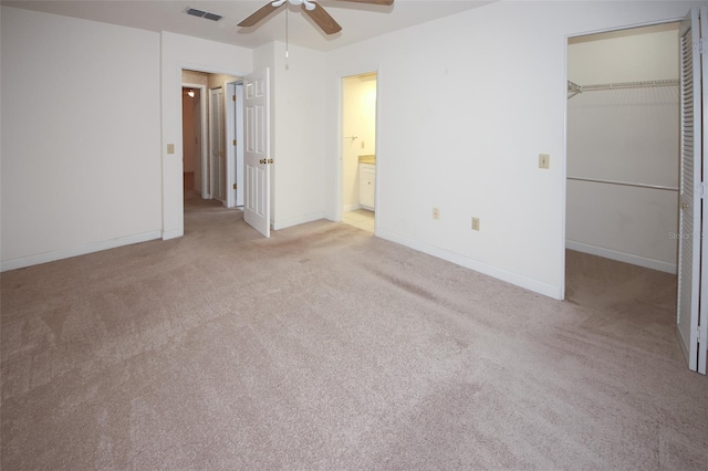 unfurnished bedroom with light carpet, a walk in closet, a closet, and ceiling fan