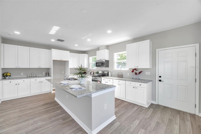 kitchen with light stone countertops, stainless steel appliances, a kitchen island with sink, light hardwood / wood-style flooring, and white cabinetry