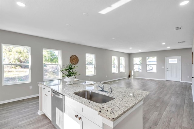 kitchen with white cabinets, a center island with sink, sink, stainless steel dishwasher, and light stone counters