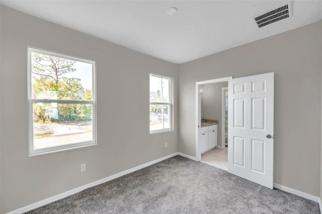 unfurnished bedroom featuring ensuite bathroom and light carpet