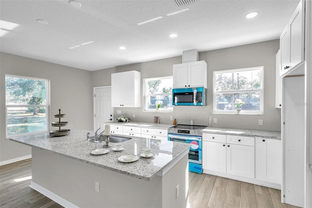 kitchen featuring light stone countertops, sink, an island with sink, white cabinets, and appliances with stainless steel finishes