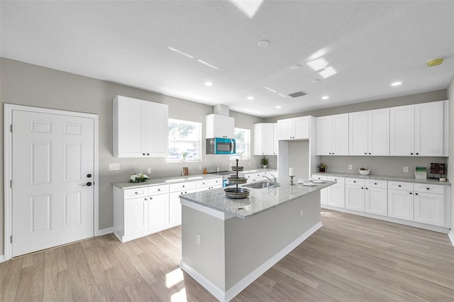 kitchen featuring white cabinets, sink, an island with sink, light hardwood / wood-style floors, and light stone counters