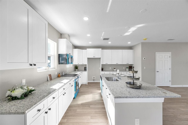 kitchen with light stone counters, a center island with sink, white cabinets, and stainless steel range with electric cooktop