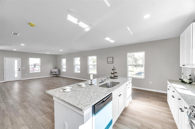 kitchen featuring light stone counters, dishwashing machine, sink, white cabinets, and an island with sink