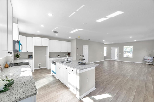 kitchen with light stone counters, a center island with sink, white cabinets, and sink