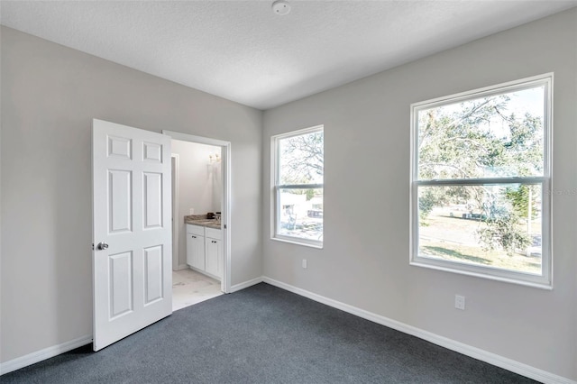 unfurnished bedroom featuring ensuite bath, light colored carpet, and a textured ceiling