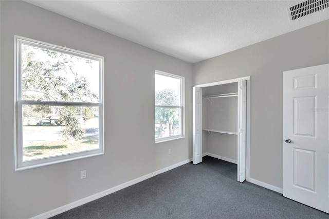 unfurnished bedroom with a closet, dark carpet, and multiple windows