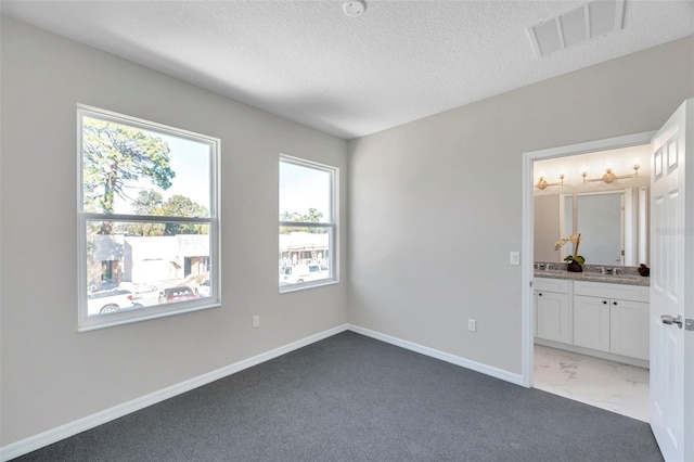 unfurnished bedroom with dark colored carpet, a textured ceiling, sink, and ensuite bath