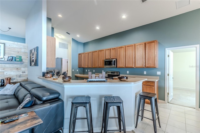 kitchen featuring appliances with stainless steel finishes, a kitchen bar, wood walls, kitchen peninsula, and light tile patterned floors