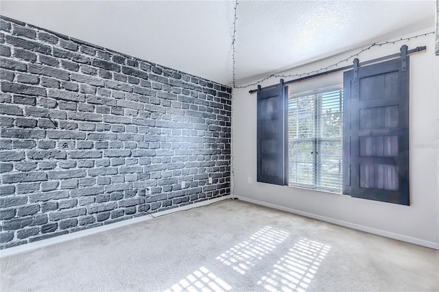 carpeted spare room with a barn door, brick wall, and a textured ceiling