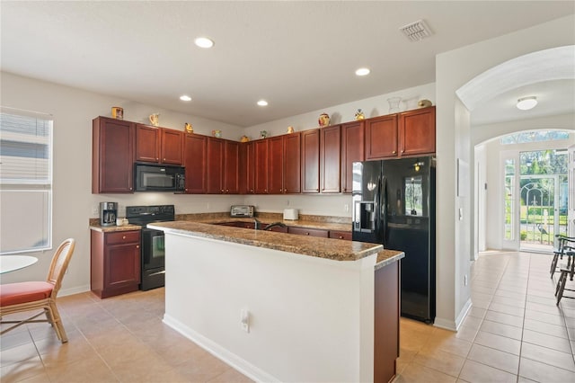 kitchen with light tile patterned flooring, stone countertops, black appliances, and an island with sink