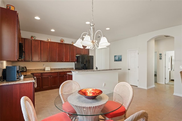 kitchen featuring a notable chandelier, pendant lighting, a center island, black fridge with ice dispenser, and light stone counters