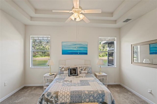 carpeted bedroom with ceiling fan and a raised ceiling