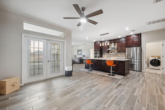 kitchen with a kitchen island with sink, pendant lighting, stainless steel fridge with ice dispenser, washer / dryer, and a breakfast bar