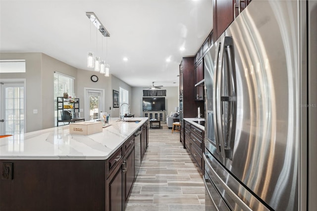 kitchen featuring decorative light fixtures, a kitchen island with sink, stainless steel refrigerator with ice dispenser, and sink