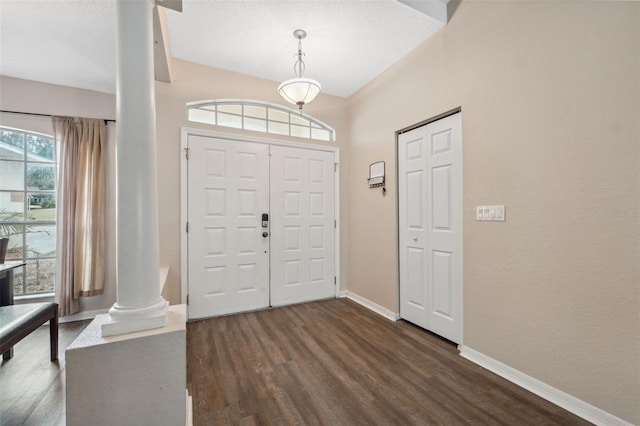 foyer entrance featuring ornate columns, a textured ceiling, and dark wood-type flooring