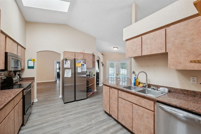 kitchen featuring appliances with stainless steel finishes, light wood-type flooring, french doors, vaulted ceiling with skylight, and sink