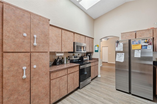 kitchen with appliances with stainless steel finishes, light hardwood / wood-style flooring, a skylight, and high vaulted ceiling