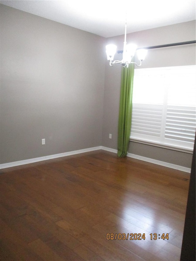 empty room featuring dark wood-type flooring and a notable chandelier