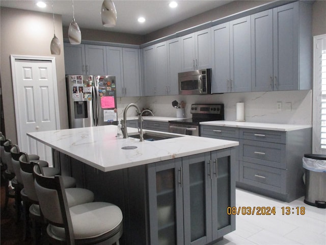 kitchen featuring gray cabinetry, a kitchen island with sink, sink, and appliances with stainless steel finishes