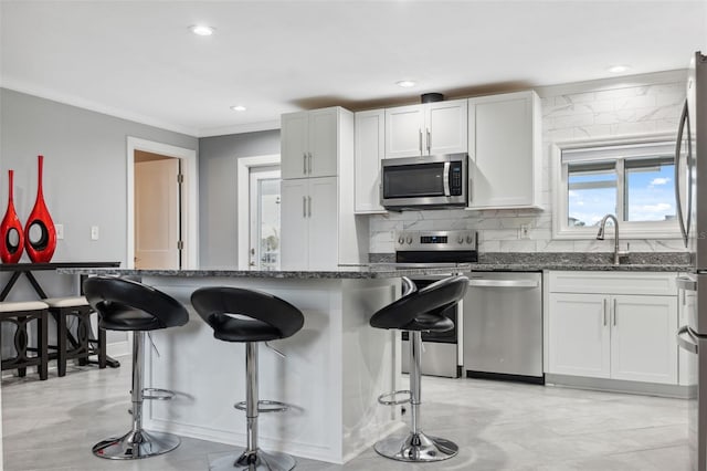 kitchen featuring sink, white cabinetry, a kitchen bar, dark stone countertops, and appliances with stainless steel finishes