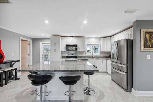 kitchen with appliances with stainless steel finishes, dark stone counters, a kitchen island, and sink