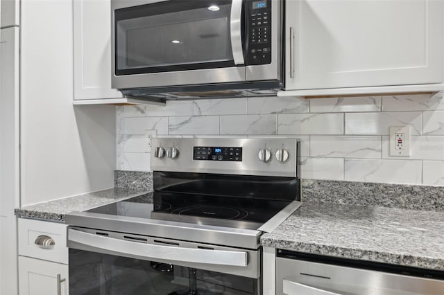 kitchen with stainless steel appliances, light stone countertops, white cabinets, and tasteful backsplash