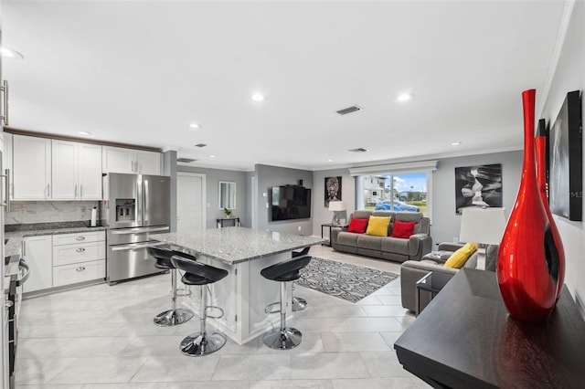 kitchen with white cabinetry, a kitchen breakfast bar, tasteful backsplash, range, and stainless steel refrigerator with ice dispenser