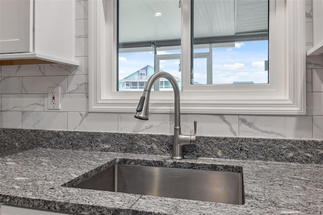 room details with stone counters, white cabinetry, backsplash, and sink