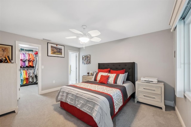 bedroom featuring ceiling fan, a walk in closet, a closet, and light colored carpet