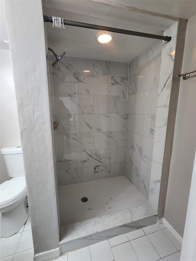 bathroom featuring tile patterned flooring, a tile shower, and toilet