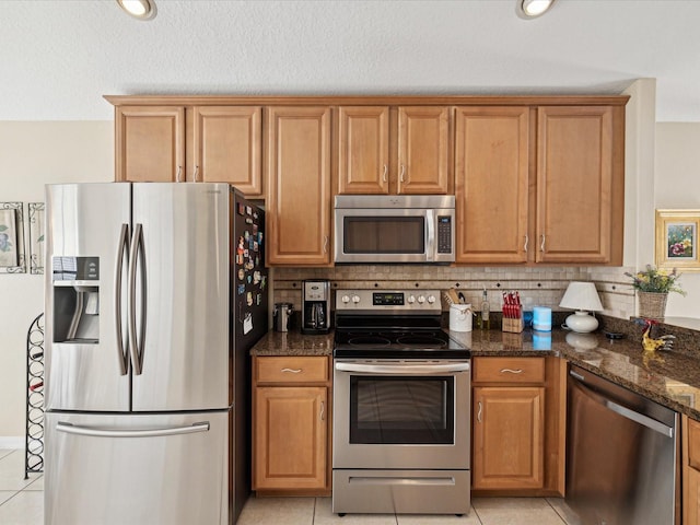 kitchen with tasteful backsplash, appliances with stainless steel finishes, light tile patterned floors, and dark stone countertops