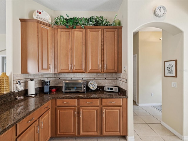 kitchen with light tile patterned floors, dark stone countertops, and tasteful backsplash