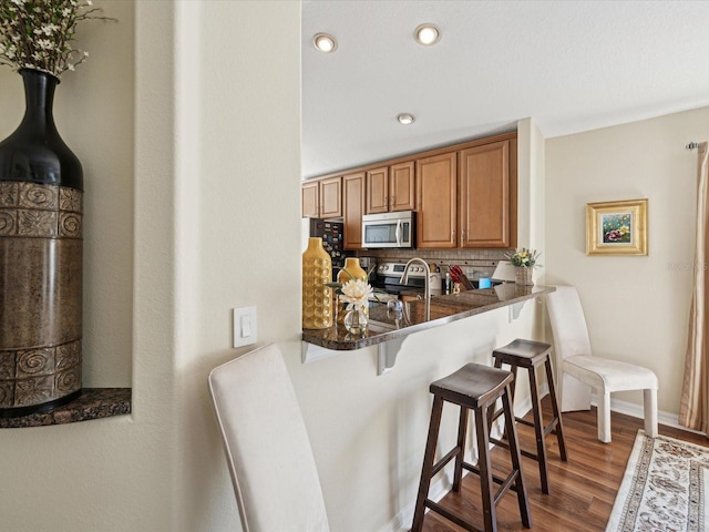 kitchen featuring kitchen peninsula, stainless steel appliances, a kitchen bar, decorative backsplash, and dark hardwood / wood-style flooring