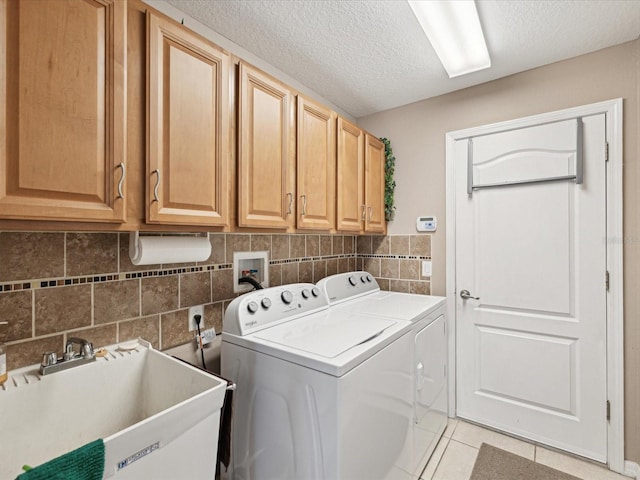 laundry room featuring light tile patterned flooring, washer and dryer, sink, cabinets, and a textured ceiling