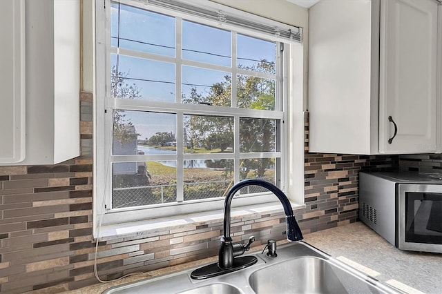 room details featuring white cabinets, a water view, backsplash, and sink