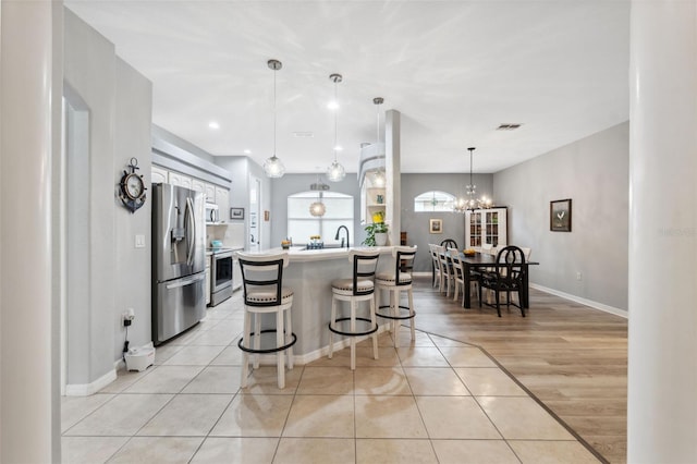 kitchen featuring stainless steel appliances, a center island, a breakfast bar, decorative light fixtures, and light tile patterned flooring