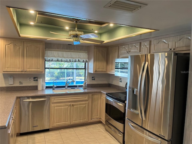 kitchen with stainless steel appliances, a tray ceiling, ceiling fan, sink, and light tile patterned floors