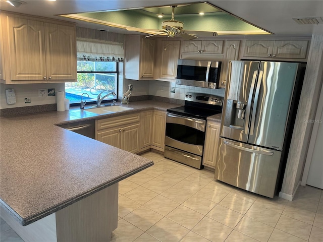 kitchen featuring sink, kitchen peninsula, a tray ceiling, light tile patterned flooring, and appliances with stainless steel finishes