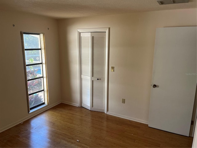 unfurnished bedroom with hardwood / wood-style floors, a closet, and multiple windows