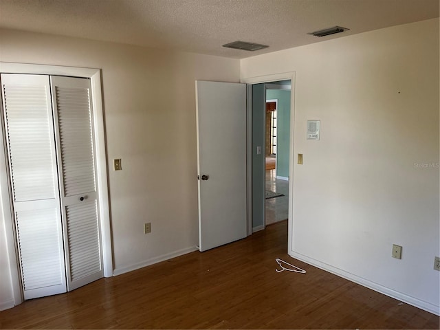 unfurnished bedroom with a textured ceiling, dark hardwood / wood-style floors, and a closet