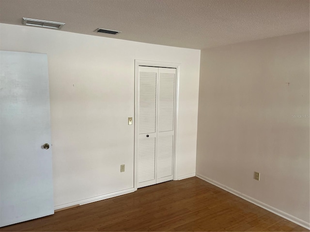 unfurnished bedroom with dark hardwood / wood-style flooring, a textured ceiling, and a closet