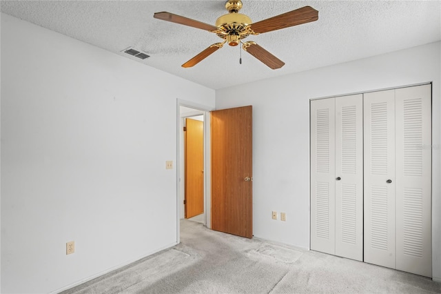 unfurnished bedroom featuring ceiling fan, a closet, light carpet, and a textured ceiling